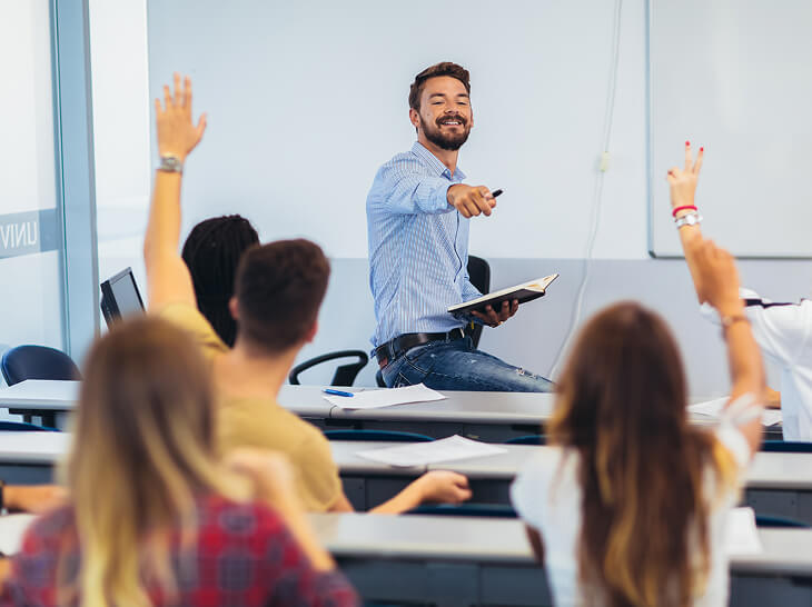 Male teacher pointing at student with hand raised