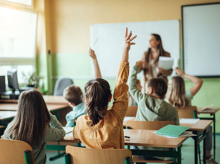 young students raising their hands in classroom